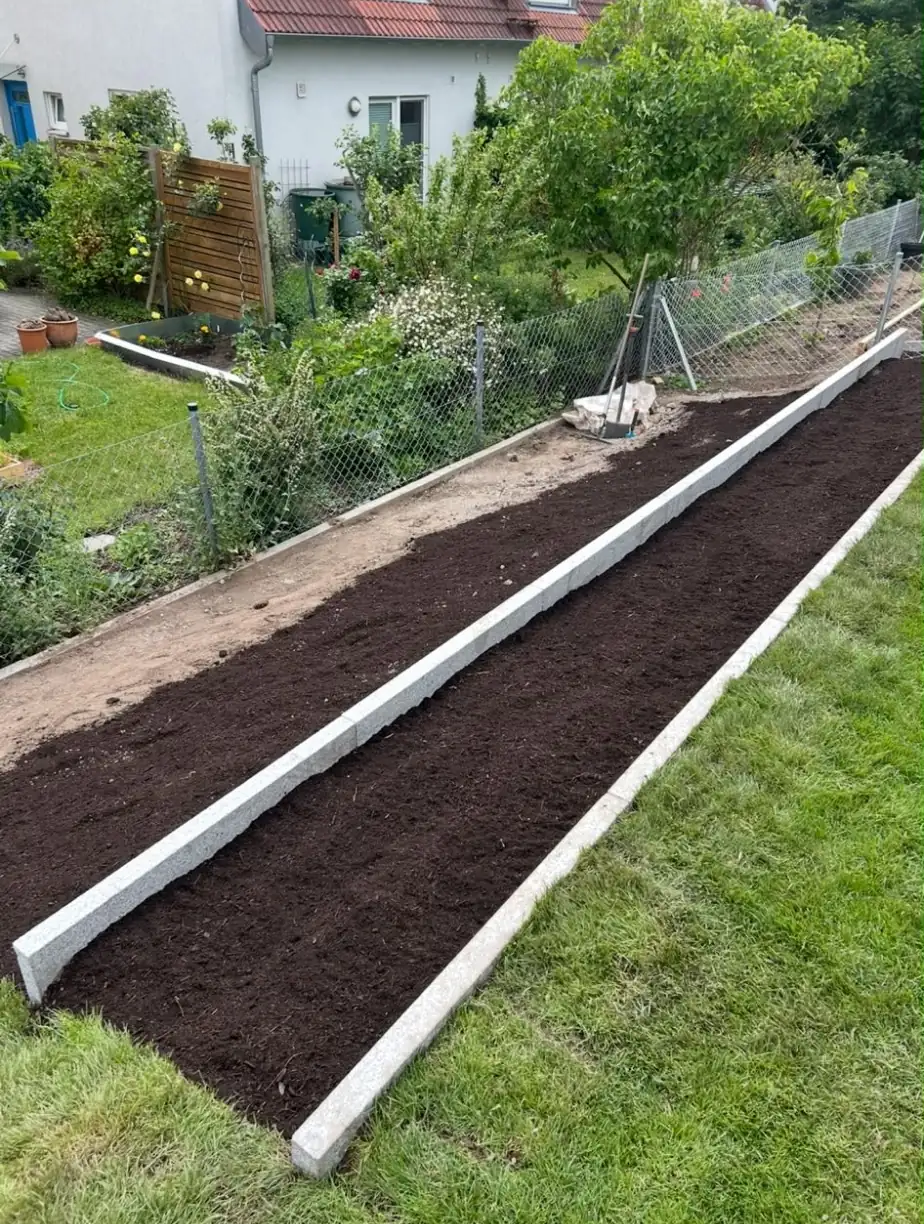 Neu angelegtes Beet mit Granit-Einfassung und frischer Erde neben dem Rasen